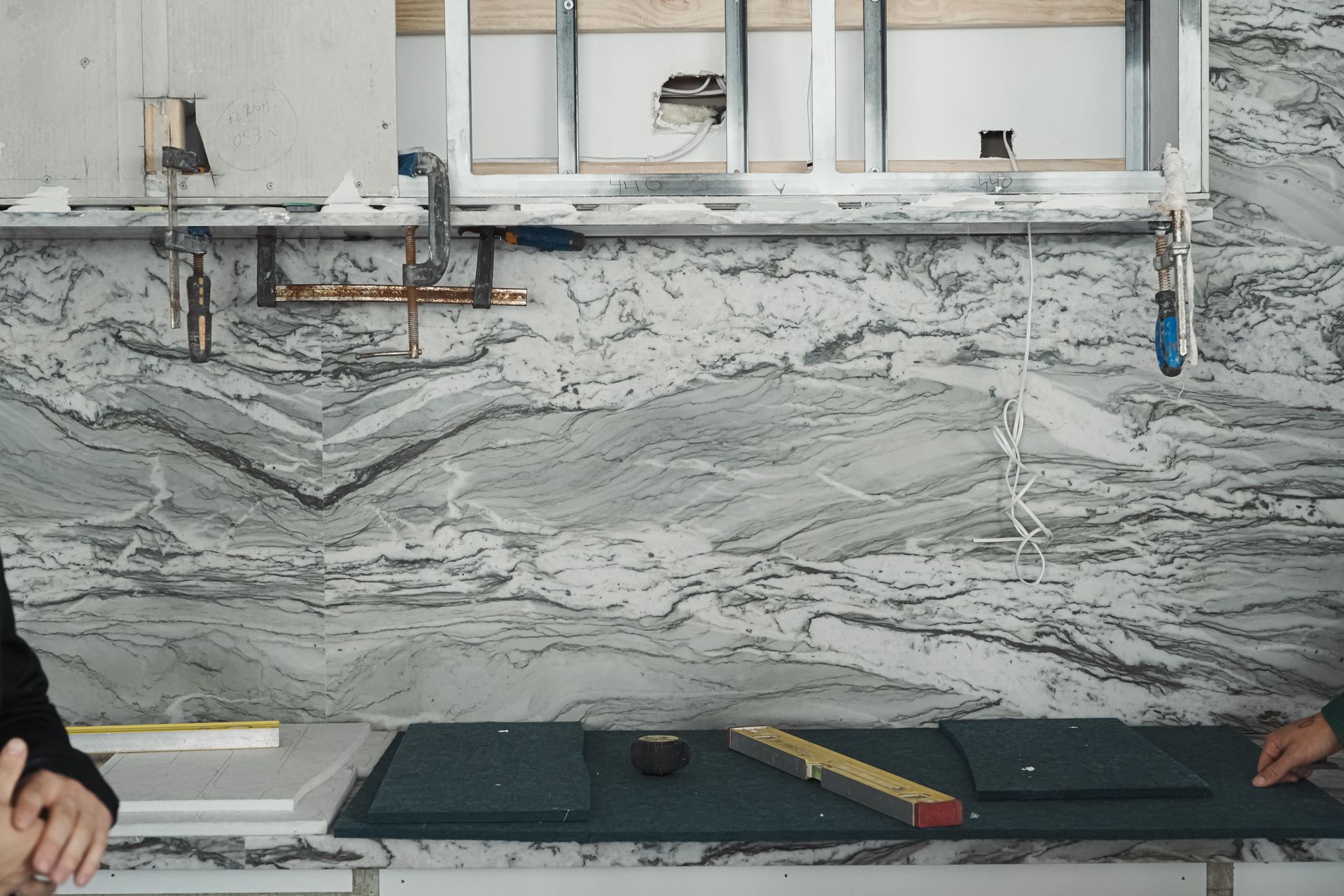 Pazzi installers securing marble benchtop with aligned cutouts for sinks and outlets using precision tools.