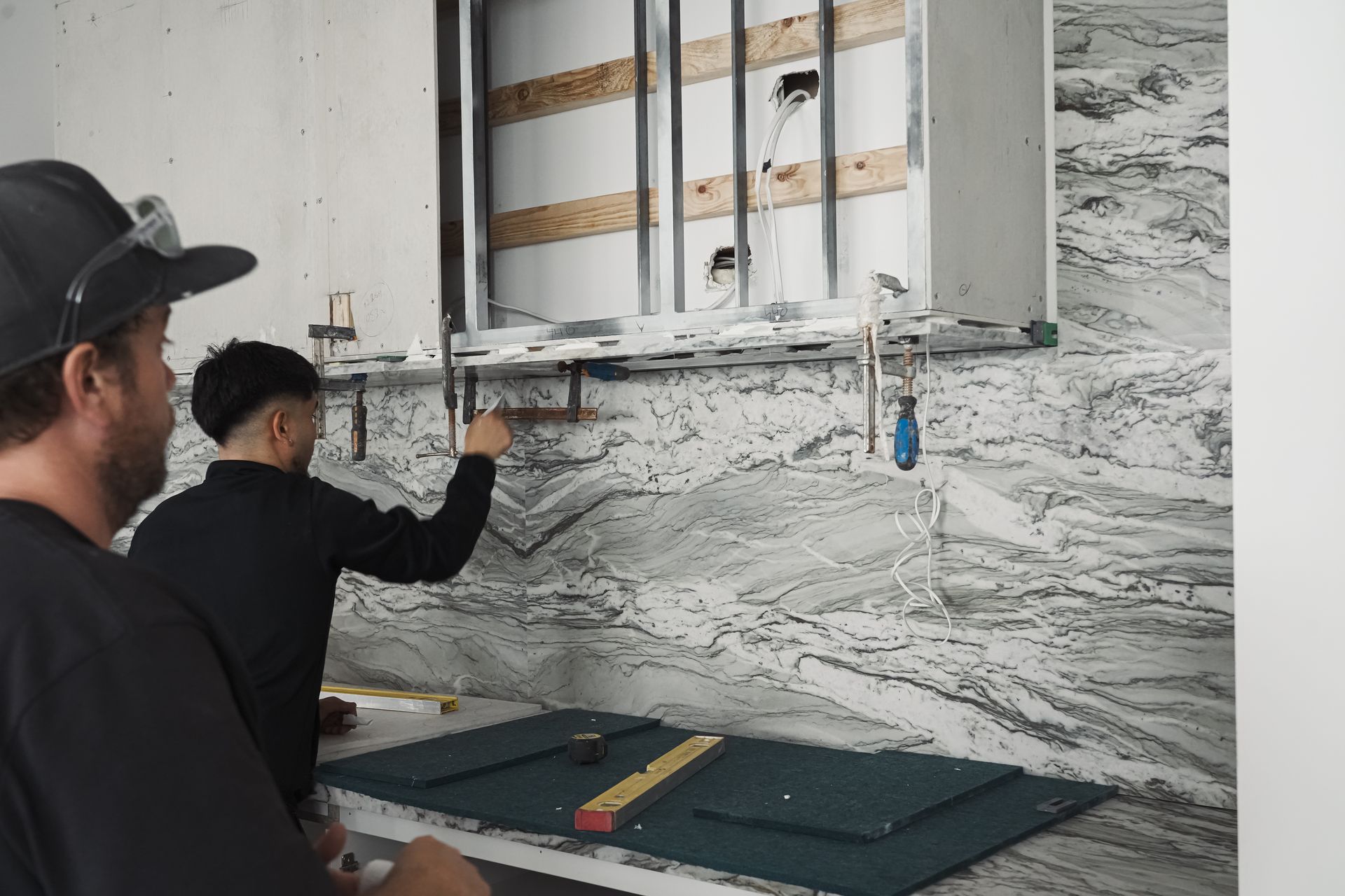 Pazzi installers securing marble benchtop with aligned cutouts for sinks and outlets using precision tools.